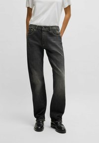 Jeans in denim nero con un taglio dritto, caratterizzati da una finitura sbiadita, cinque tasche e cuciture a contrasto. Indossati con una maglietta bianca.