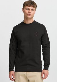 Black sweatshirt made of thick fabric, featuring a round neck, long sleeves, and a small geometric logo on the chest. Seam detailing is present.