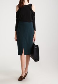 Svart blus med kall axel och volangdetaljer; mörkgrön pennkjol med slits fram; leopardmönstrade loafers; svart tote-väska.