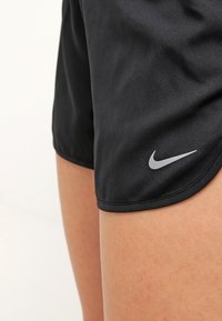 Primer plano de un muslo de una persona que lleva puestos unos pantalones cortos deportivos negros de Nike con el logo reflectante blanco de Nike en el dobladillo.