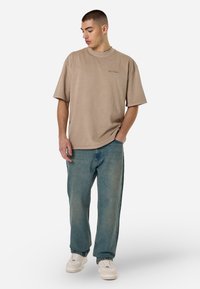 Beeži ülepaisutatud T-särk ümmarguse kaelusega, koos laia helesinise denimite otsaga ja valgete spordijalatsitega. Mustreid ega tarvikuid ei ole nähtaval.