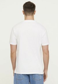 Weißes Baumwoll-T-Shirt mit kurzen Ärmeln, Rundhalsausschnitt, glatter Textur und geradem Saum. Schlichte Rückansicht, getragen mit blauen Denim-Shorts.