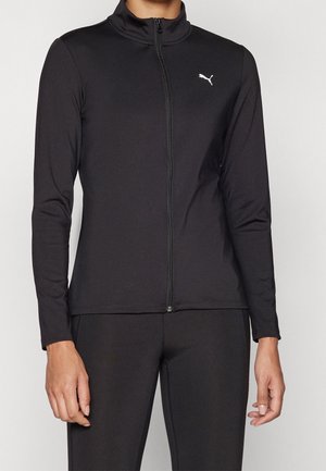 Persona vistiendo una chaqueta negra ajustada con cremallera, mangas largas y un pequeño logo blanco de Puma en el pecho izquierdo.