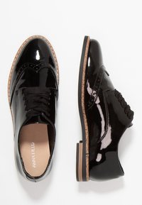 Chaussures oxford en cuir verni noir avec un laçage, des détails en brogue et une semelle en caoutchouc tan contrastante. Texture lisse, bout rond.