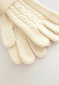 Adīti vilnas cimdi krēmkrāsā ar ribotu aproci un teksturētu kabeli uz aizmugures, kas piešķir papildu detaļas un siltumu.