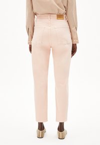 Jean droit rose clair avec quatre poches, une étiquette de marque à la taille et une texture en coton lisse. Accompagné d'un chemisier à rayures.