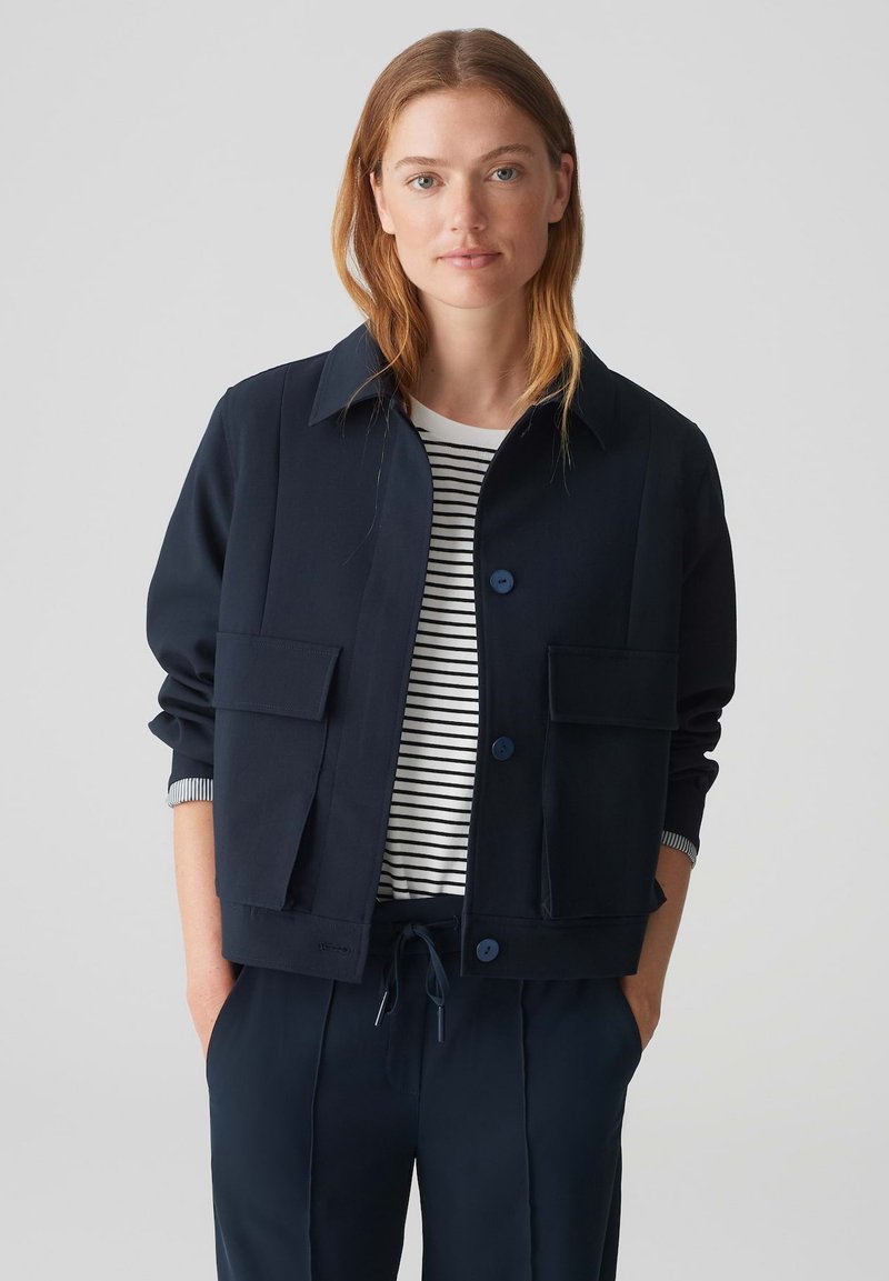 Navy blue lightweight jacket with a collar, two front pockets, and blue buttons, worn over a white and navy striped shirt.