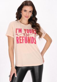 Kortærmet beige t-shirt med fed pink grafisk tekst: "JEG ER DIN ingen REFUNDERING." Materialet er blødt med rullede ærmer og en afslappet pasform.