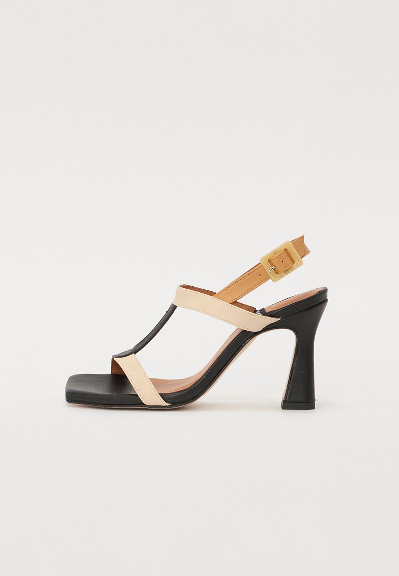 Sorte og beige høyhælte sandaler med firkantet tå. Har kryssremmer, justerbar ankelspenne, og et strømlinjeformet, minimalistisk design.