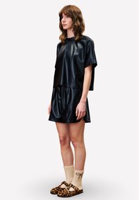 Zwarte faux leren top en bijpassende shorts met een boxy ontwerp. G gedragen met schoenen met luipaardprint en beige sokken met een strik.