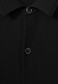 Polo shirt tricotat negru, cu un material texturat, guler și un nasture negru la guler.
