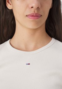 Lys beige ribbes t-skjorte med rund hals. Har et lite brodert logo i blått, rødt og hvitt på brystområdet.