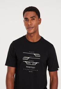 Camiseta de algodón negra con un diseño gráfico que presenta texto en blanco: "RIGHTY", "LEFTY" y "A-FRAME", junto con "PROTEST SPORTSWEAR" en la parte inferior.