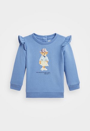 Sudadera de algodón azul con acentos de hombros con volantes, que presenta una ilustración de un oso con una camisa y una falda, y el texto "Polo Bear by Ralph Lauren".