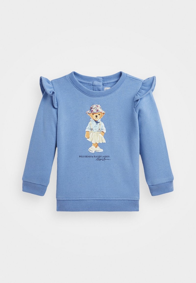 Sweatshirt en coton bleu avec des accents de volants aux épaules, présentant une illustration d'un ours portant une chemise et une jupe, et le texte "Polo Bear by Ralph Lauren".