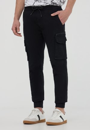Pantaloni jogger neri realizzati in tessuto morbido, dotati di numerose tasche cargo, vita elastica con cordino e polsini a costine.