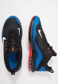 Zwarte sportieve schoenen met blauwe en rode accenten, een bovenkant van gaas en zichtbare Air-demping. Voorzien van zwarte veters en een wit swoosh-logo.