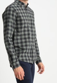 Vihreä-musta ruudullinen, pehmeästä kankaasta valmistettu nappipaita. Siinä on kaulus ja napitettu hihansuut sekä istuva leikkaus.