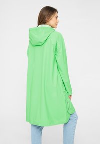 Impermeable verde con capucha, de manga larga y con detalles de botones a presión. Textura suave; llega hasta la mitad del muslo. Diseño ligero.