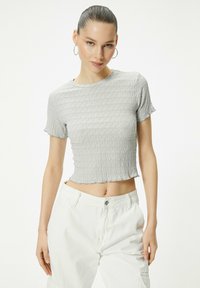 Grå cropped t-shirt med et tekstureret, bølget stofdesign, korte ærmer og rund halsudskæring, parret med hvide bukser.