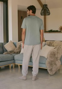 Hellgrünes T-Shirt mit kurzen Ärmeln, kombiniert mit strukturierten, hellgrauen Jogginghosen. Das Modell trägt gemütliche, neutralfarbene Socken.