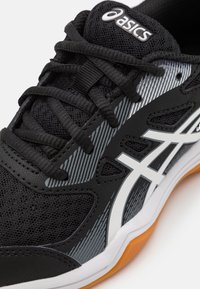 Scarpa sportiva nera con tomaia in rete, caratterizzata da accenti a strisce bianche e grigie. Suola in gomma con dettagli arancioni, con lacci in evidenza sulla parte superiore.