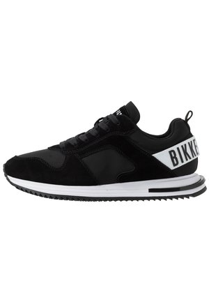 Czarny niski sneaker z białą podeszwą, wiązany i z białym paskiem na pięcie z czarnym napisem "BIKK" po boku.