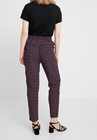 Černý top s krátkým rukávem spárovaný s úzkými kalhotami s květinovým vzorem v růžové, bílé a fialové barvě a elastickým pasem.