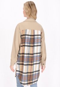 Beige szőtt elülső résszel és puha kockás hátsó résszel készült tunika, barna, kék és fehér árnyalatokban, galléros nyakkal és hosszú ujjal.