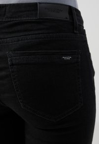 Juodos džinsinės kelnės su galiniais kišenėmis. Savybėje yra odinė etiketė su užrašu "Marc O'Polo DENIM." Paprastas siuvinėjimas ir lygus paviršius.