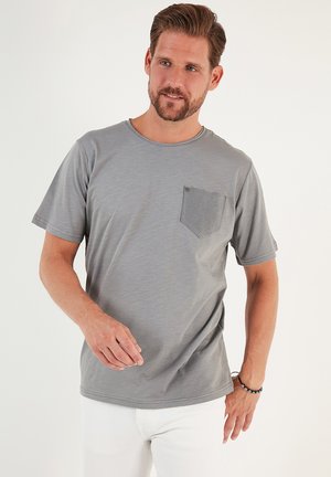 Camiseta gris de manga corta hecha de una tela suave, con un bolsillo de parche texturizado en el lado izquierdo y un escote redondo.