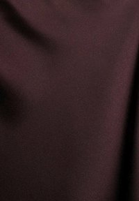 Donker paarse gladde stof met subtiele plooien en schaduwen die textuur en val tonen.