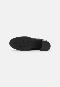 Suela de zapato negra con un patrón de agarre texturizado, que presenta indentaciones rectangulares para tracción y una sección de talón curvada para estabilidad.