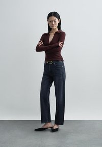 Bordo spalvos iškirptas V formos kaklu ilgarankoviai megztinis su juostelėmis, derinamas su tamsaus džinso tiesių kelnių sąvaržomis ir juodais smailiais bateliais, ant vienalytės fono.