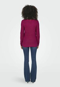 Pull à manches longues magenta avec un col rond, présentant un motif de tricot texturé et un ourlet arrière légèrement plus long, associé à un jean bleu foncé évasé.