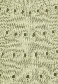 Ljusgrön stickad tyg med en ribbad rund halsringning och små hål som skapar ett strukturerat, öppet mönster.