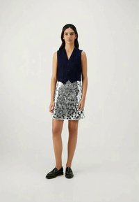 Ναυτικό κοντομάνικο γιλέκο με στρογγυλά κουμπιά, σε συνδυασμό με μια ασημένια φούστα παγιέτα με τελεία σχέδιο. Μαύρα μοκασίνια ολοκληρώνουν την εμφάνιση.