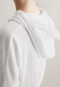 Witte katoenen hoodie met een zachte, gedrapeerde capuchon. De stof lijkt lichtgewicht met een gladde textuur en toont de achterkant en de halslijn.