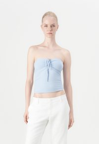 Top azul claro sem alças com um detalhe de laço na frente. Tecido suave, design ajustado. Combinado com calças brancas de cintura alta. Estilo minimalista.