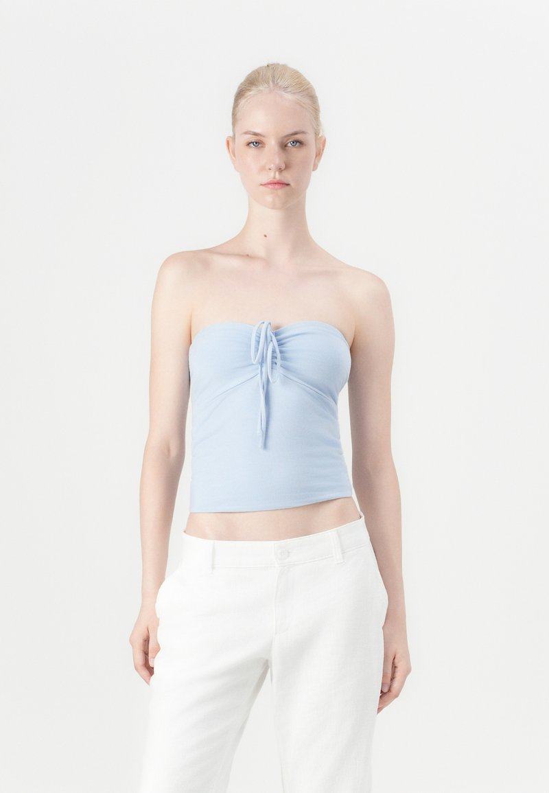 Top azul claro sem alças com um detalhe de laço na frente. Tecido suave, design ajustado. Combinado com calças brancas de cintura alta. Estilo minimalista.