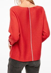 Pull rouge en maille avec un col carré, présentant une couture verticale blanche contrastante dans le dos et des manches longues légèrement amples.