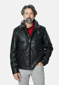 Chaqueta de cuero negra con un collar de piel sintética gris, con dos bolsillos frontales, cierre de cremallera y una textura suave. Llevada sobre una camisa roja.