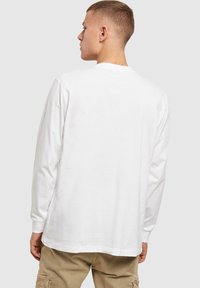 Hvid langærmet T-shirt med rund hals og løs pasform. Fremstillet af bomuld, har et simpelt design og lige bundslå. Ingen mønstre.