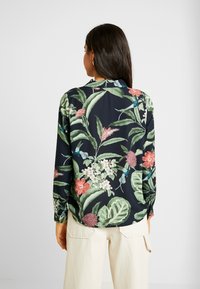 Camicia a maniche lunghe di un blu navy scuro con vivaci motivi floreali e fogliari. Tessuto morbido, colletto e vestibilità leggermente ampia, con accenti colorati.