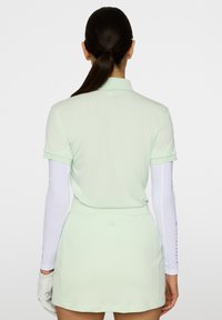 Vaaleanvihreä lyhythihainen polo-paita, joka on yhdistetty samanväriseen hameeseen. Pitkä valkoinen aluspaidat ja käsineet ovat esillä. Minimalistinen muotoilu.