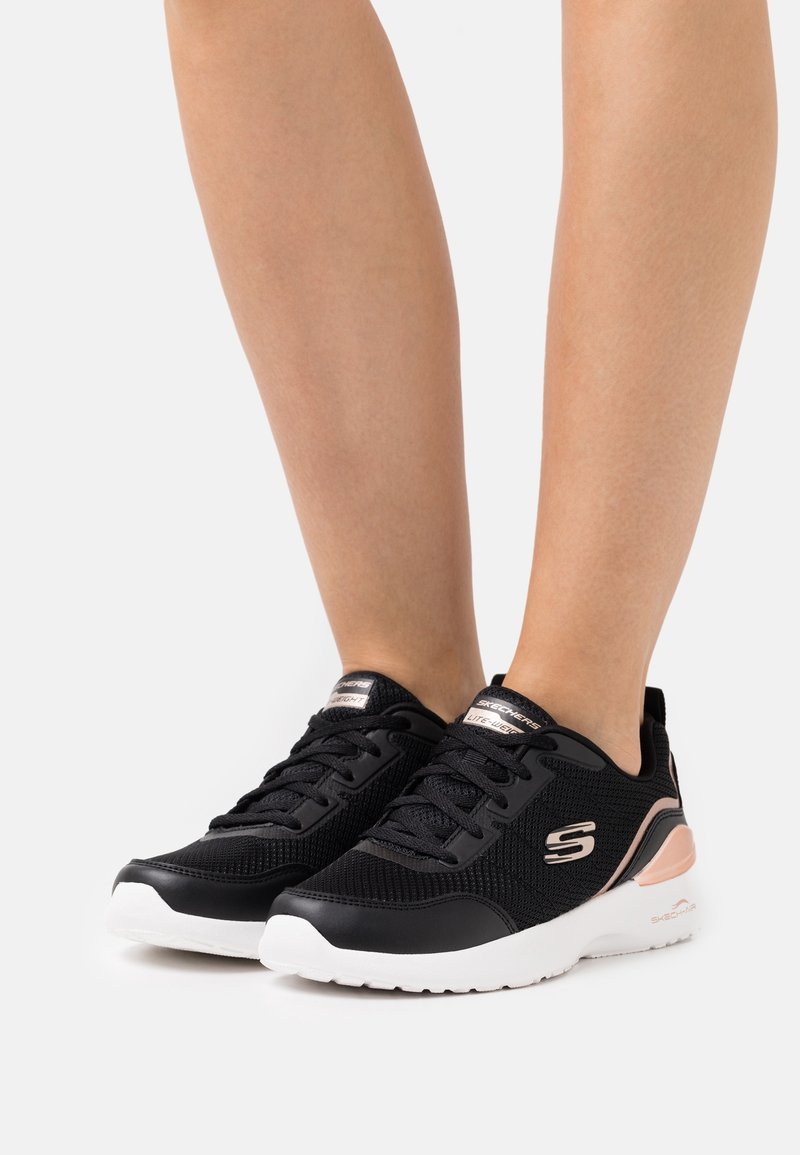 Schwarze Sportschuhe mit einer strukturierten Mesh-Oberfläche, ausgestattet mit schwarzen Schnürsenkeln und einer weißen Sohle mit pinkem Akzent an der Ferse.