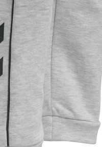 Grauer Pullover mit glatter Textur, einem großen schwarzen Grafikdesign auf der Vorderseite und einem kontrastierenden schwarzen Saum entlang der Nähte.