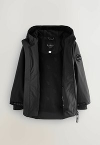 Schwarze Jacke mit abnehmbarer Kapuze, einem gefütterten Innenraum aus Fleece und gesticktem Logo auf dem Ärmel. Beinhaltet einen Reißverschluss und verstellbare Ärmelabschlüsse.