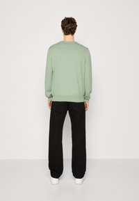 Myntgrön tröja med lång ärm och ribbade manschetter, bärs tillsammans med svarta byxor och vita sneakers. Tyget ser mjukt och texturerat ut.