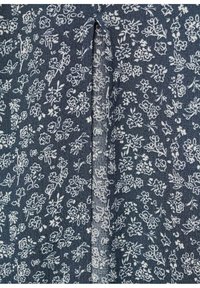 Blått tyg med ett vitt blommönster. Har små blommor och blad, vilket visar en mjuk, texturerad yta med en veckdetalj.